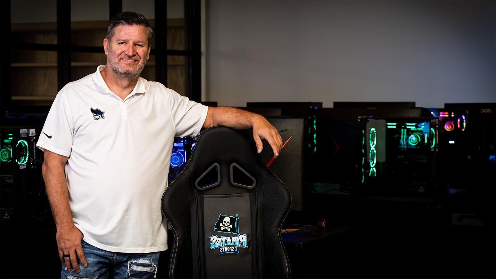 Scott Brumfield stands in front of gaming PCs. 他坐在PSC海盗队的游戏椅旁边，穿着海盗队的球衣.