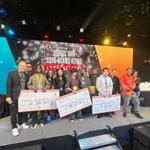 Techfest tournament winners holding large scholarship checks on stage alongside 满帆 staff members in the Fortress.